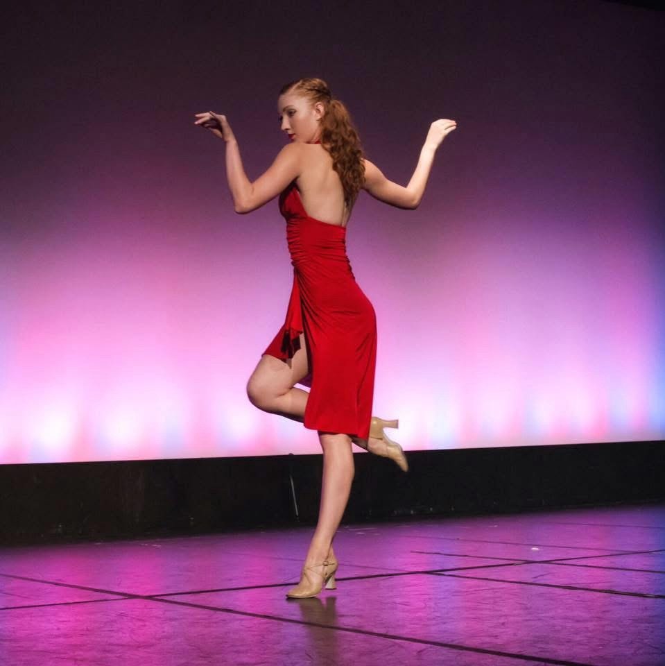 Solo on stage in a deep-red halter dress, balanced in passé