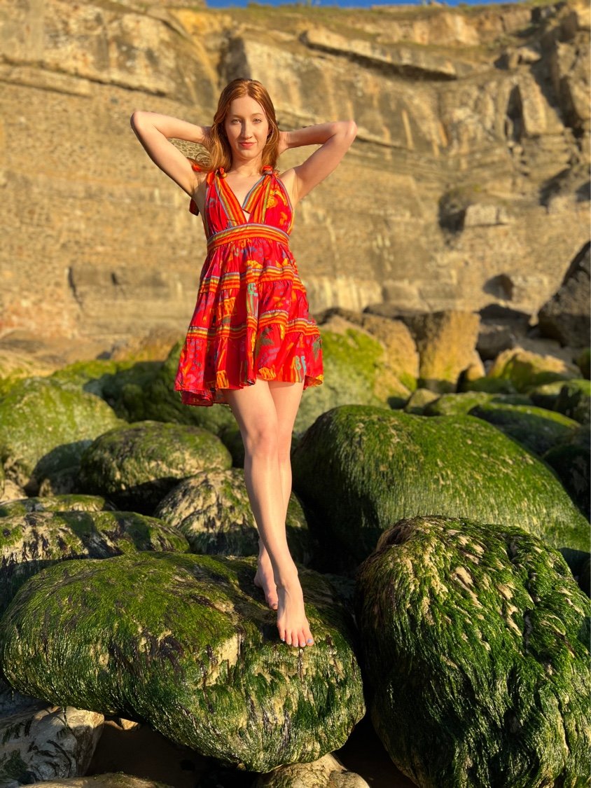 Melissa on mossy beach rocks at golden hour, red sundress