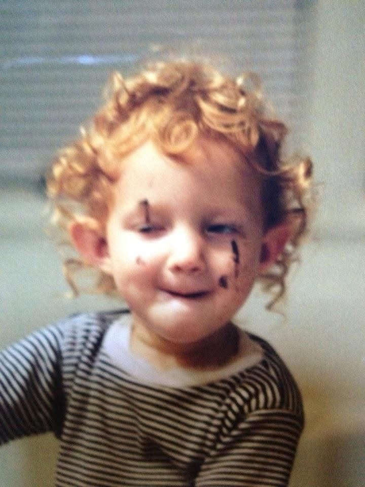 Curly-haired redhead toddler in a striped top with chocolate streaked on her cheek