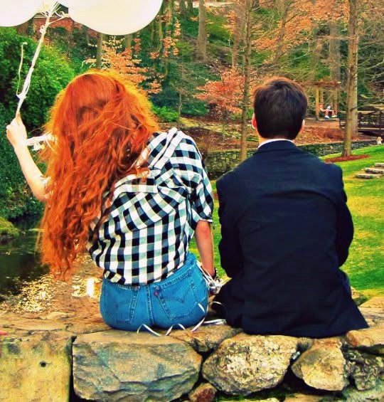 Couple from behind on a stone wall in an autumn park, holding white balloons