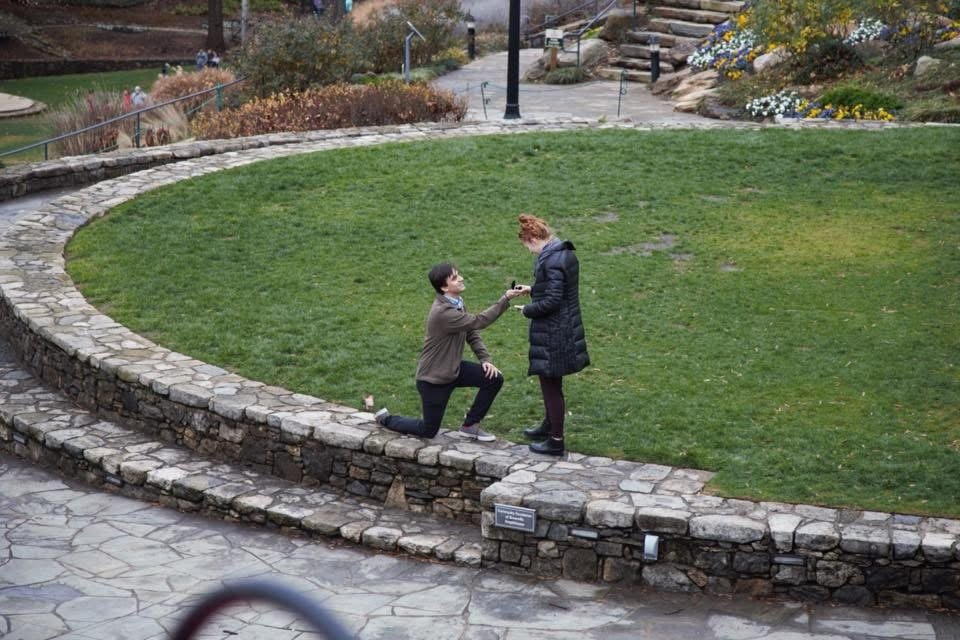 Proposal in a stone-walled garden overlook, boyfriend on one knee