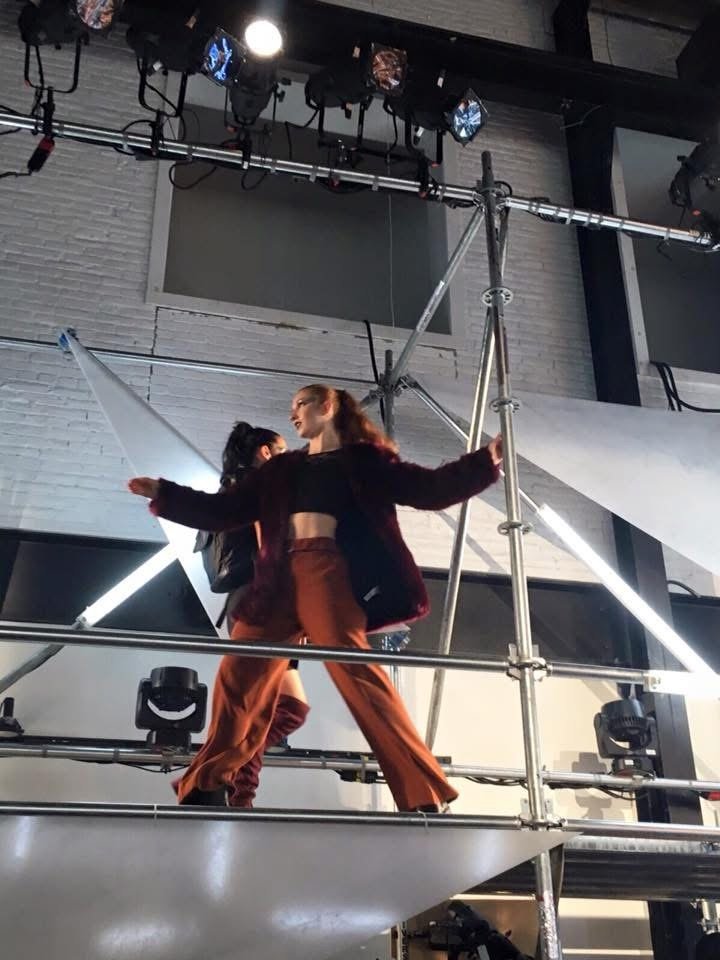 On a steel scaffold rig in a photo studio, burgundy coat and rust pants